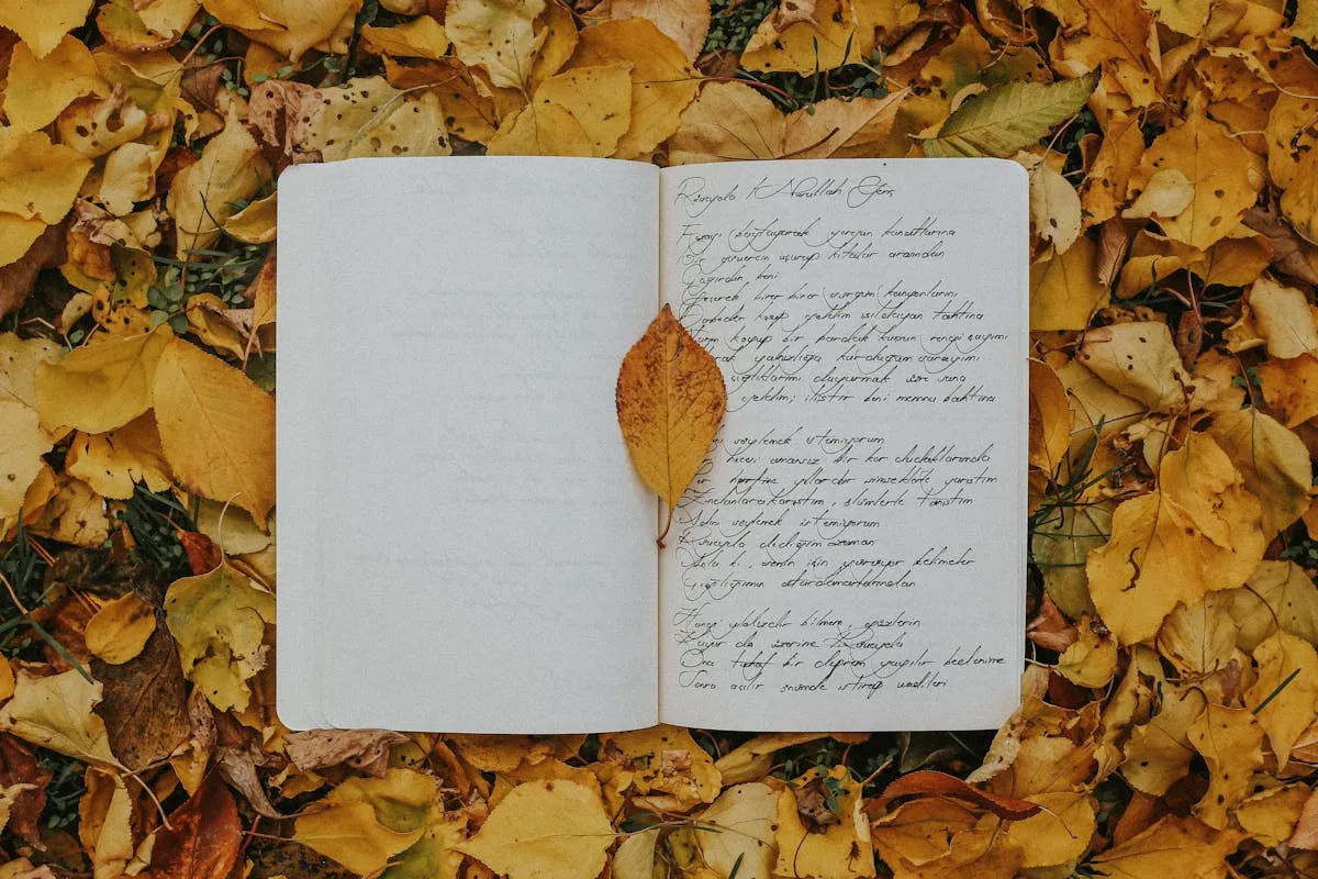 Open notebook with cursive handwriting resting on a bed of yellow autumn leaves outdoors