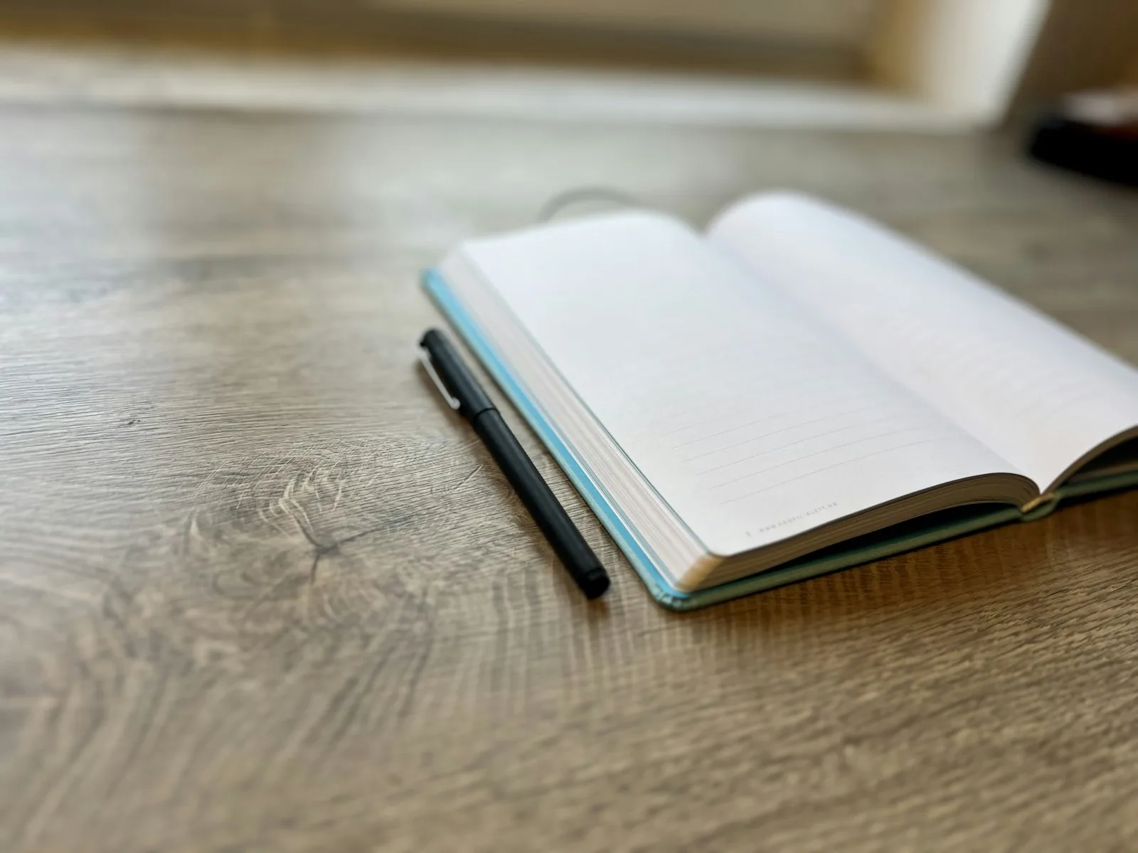 An open bullet journal with a dot grid page and a pen on a wooden desk