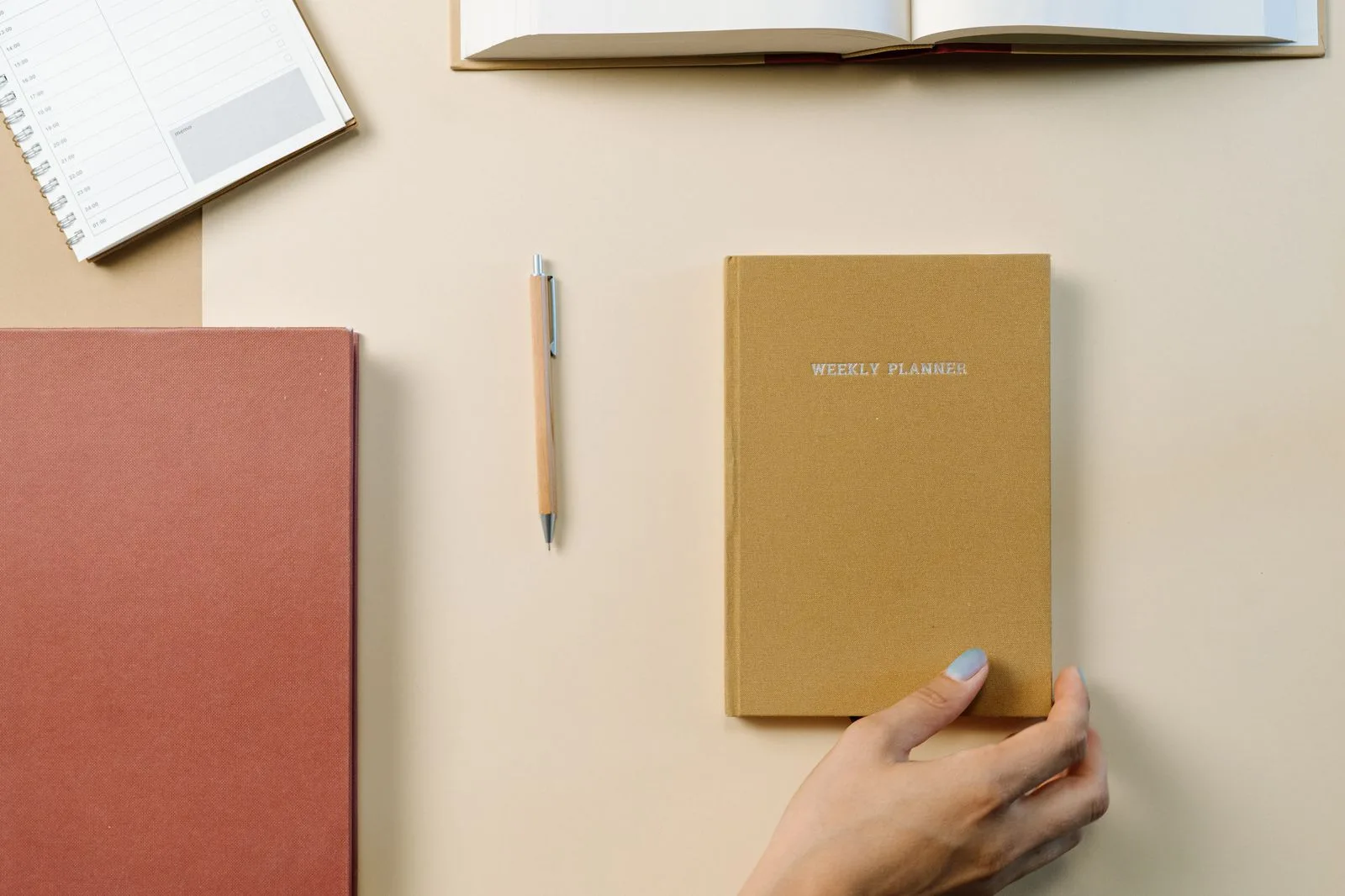 Several notebooks and planners with a pen on a warm neutral desk