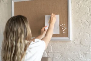 Cork Board Vision Board: Why Pinning Beats Gluing (and How to Set One Up) Woman pinning a photograph onto a wall-mounted framed cork vision board