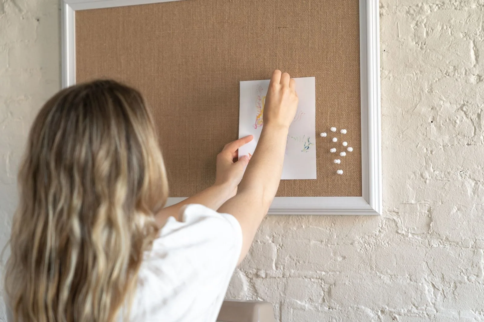 Woman pinning a photograph onto a wall-mounted framed cork vision board