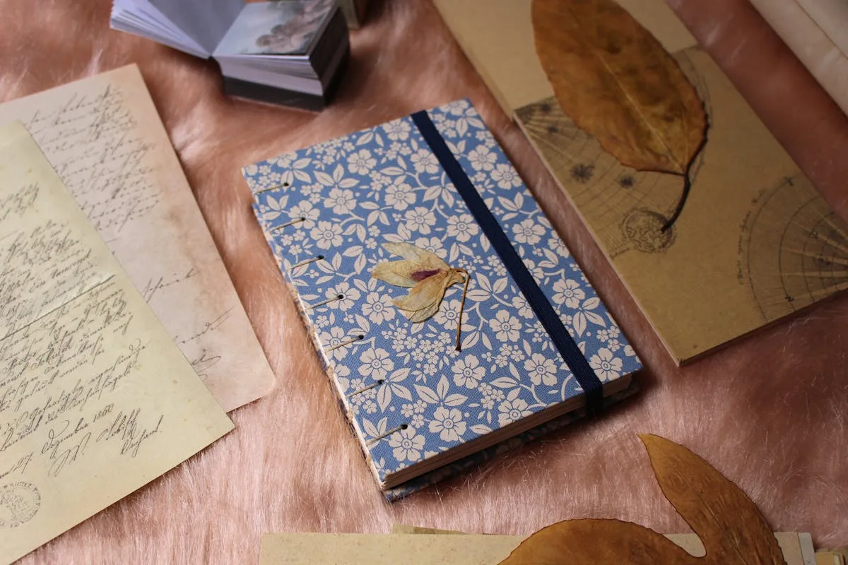 Blue floral fabric junk journal cover with a pressed leaf among vintage letters