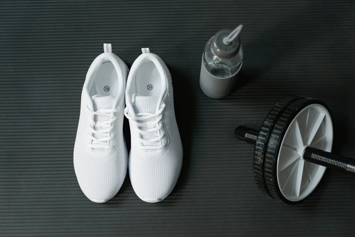 Flat lay of white running shoes, a water bottle, and an ab roller on a gym mat