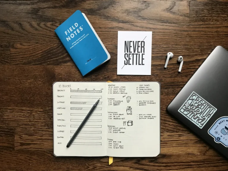 Handwritten fitness tracker journal with a pencil beside a laptop on a wooden desk