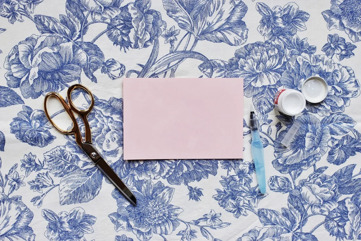 Glue, scissors, and paper arranged on a floral background for paper crafts