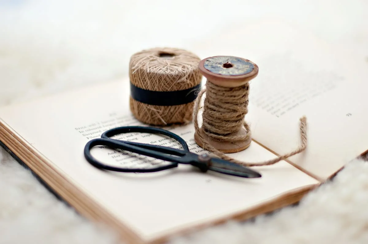 Twine spool, scissors, and natural cord arranged on an open book in soft natural light