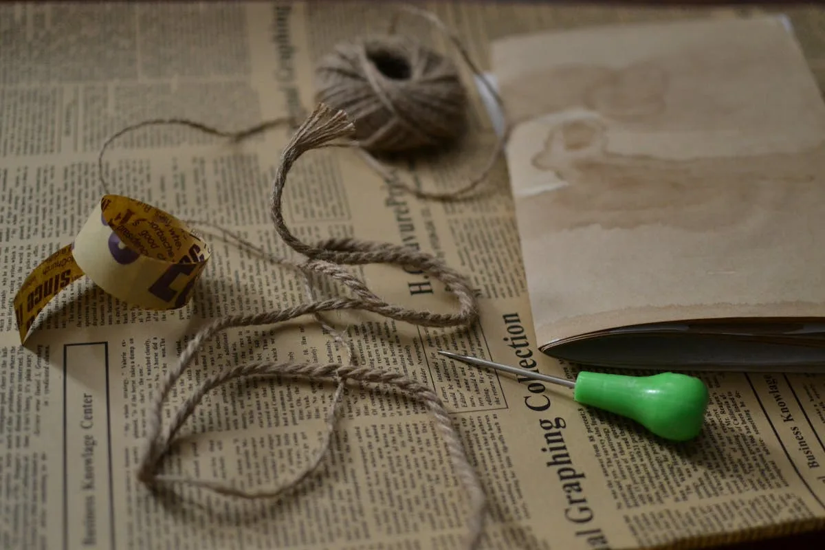 Twine, an awl, and torn paper laid on a newspaper background, ready for bookbinding