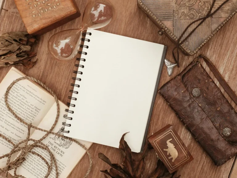 Stack of cream-colored handmade journals open and closed on a white surface with a vintage book and brass paper clip