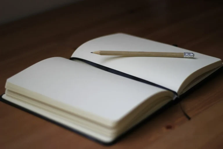 Open blank journal spread with a pencil resting on warm wooden desk, ready for a junk journal entry