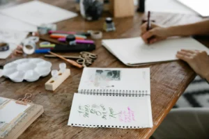 Warm wooden craft desk with journaling supplies and hands lettering in a notebook
