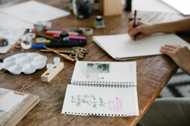 Warm wooden craft desk with journaling supplies and hands lettering in a notebook