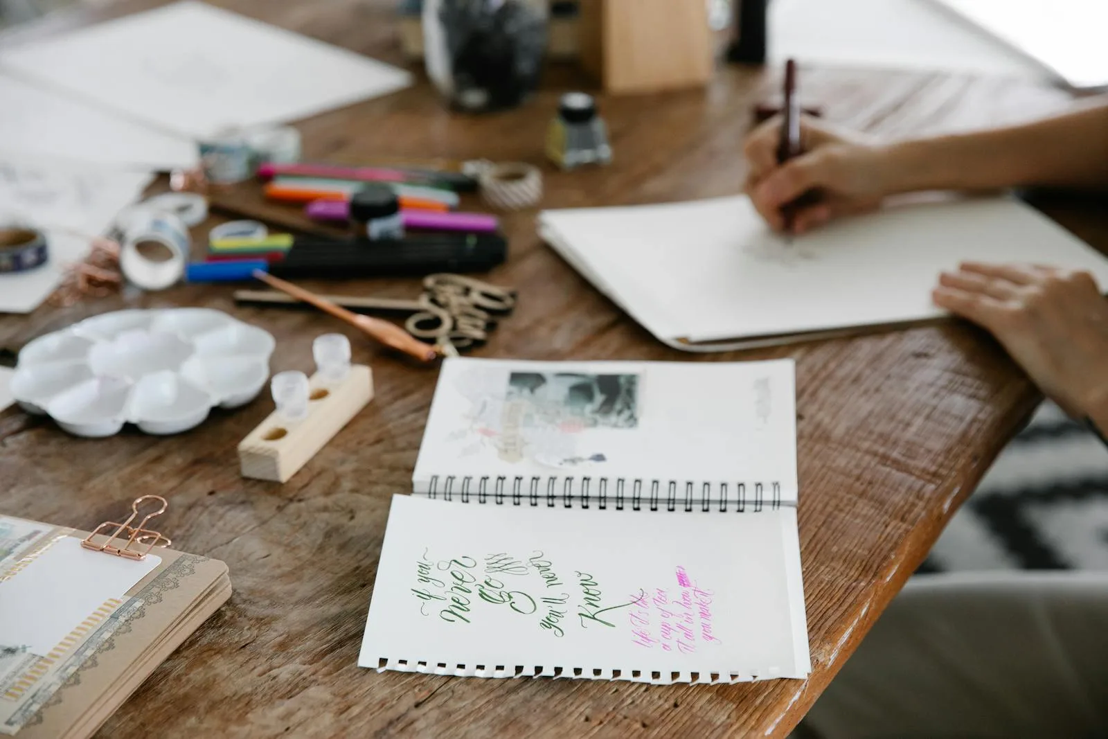 Warm wooden craft desk with journaling supplies and hands lettering in a notebook