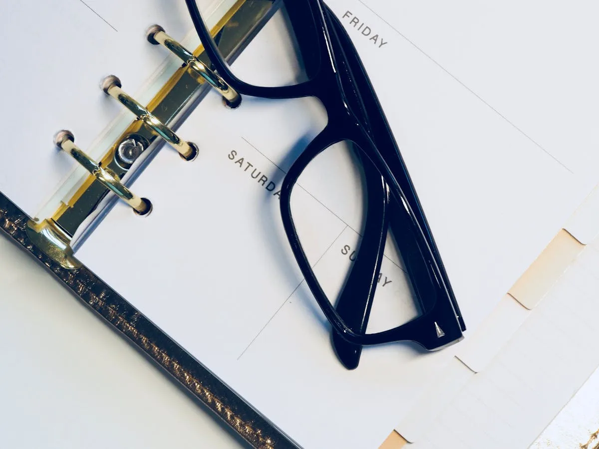 Ring-bound planner open to daily pages with reading glasses resting on top
