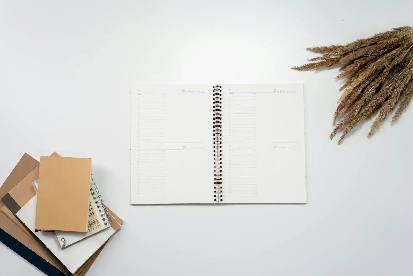 Open weekly planner notebook on a white desk beside a stack of kraft notebooks