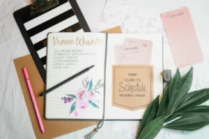 Free Printable Wedding Planner: Build a Whole Binder Without the $50 Book Open wedding planning notebook with venue checklists, a pink pen and greenery