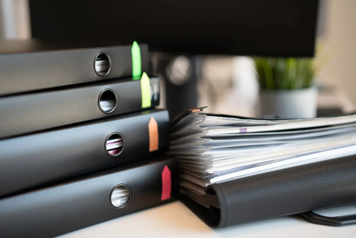 Stack of ring binders with colored tab markers and a folder of papers on a desk