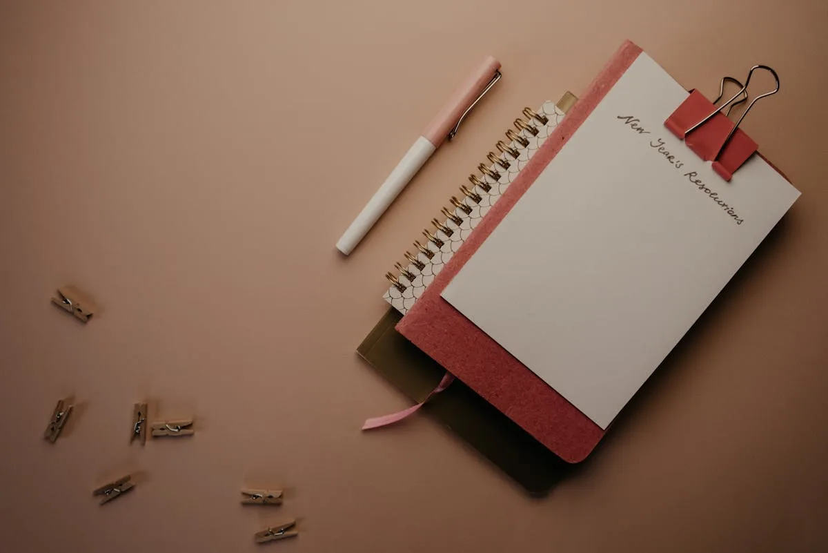 A spiral notebook clipped to a pad of paper with a New Year Resolutions header in a neutral palette