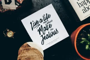 Handwritten quote card on a desk surrounded by small home objects and a vintage clock