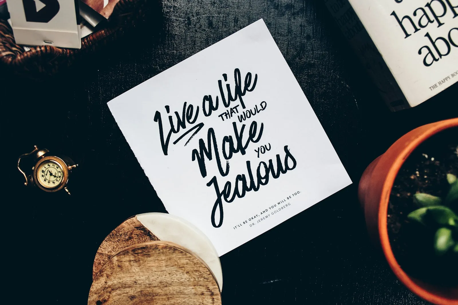 Handwritten quote card on a desk surrounded by small home objects and a vintage clock