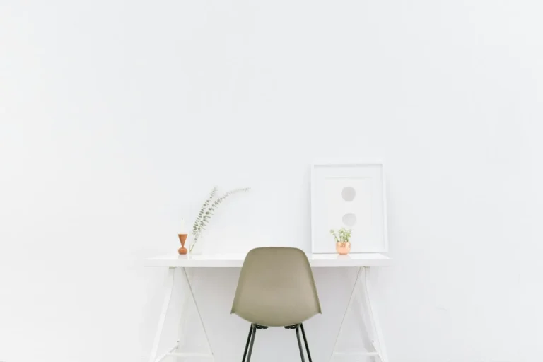 Minimal white desk with a book, plant and chair in soft light