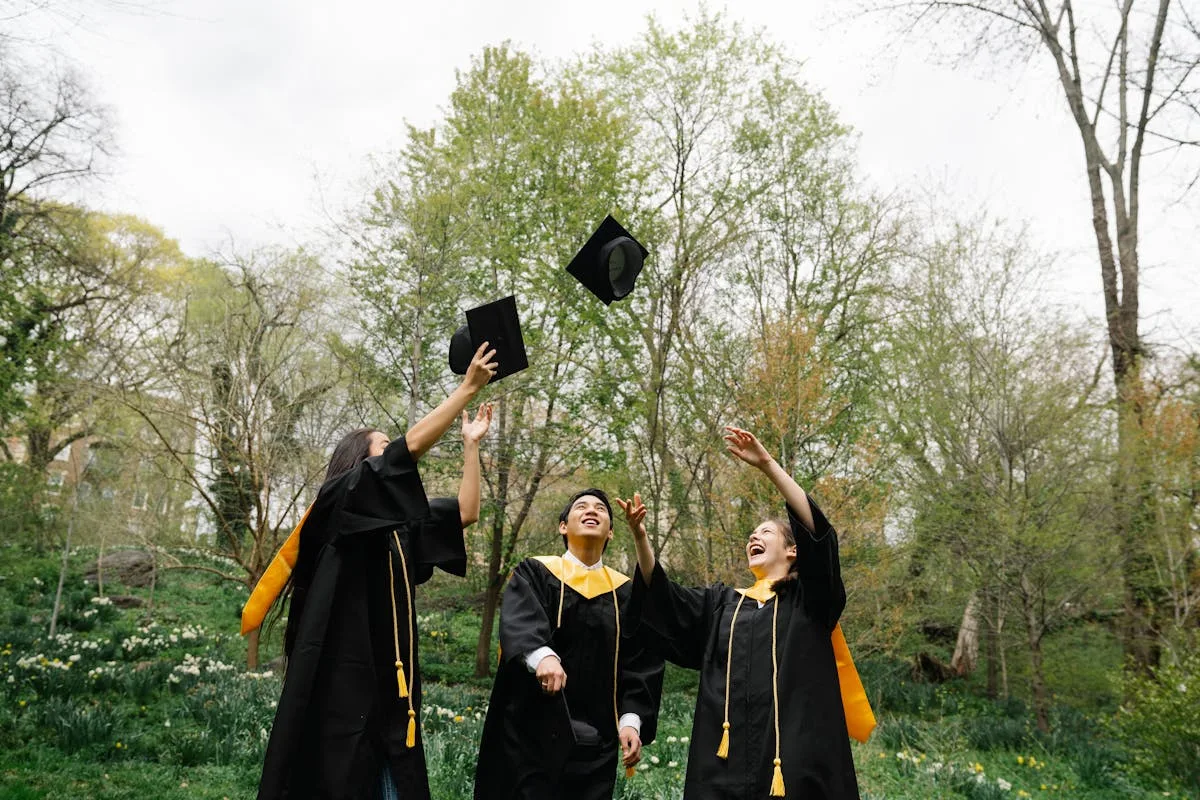 Three graduates in gowns tossing their caps in the air to celebrate
