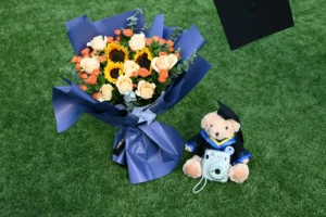 Graduation bouquet, a black cap, and a teddy bear in a cap and gown laid out as keepsakes