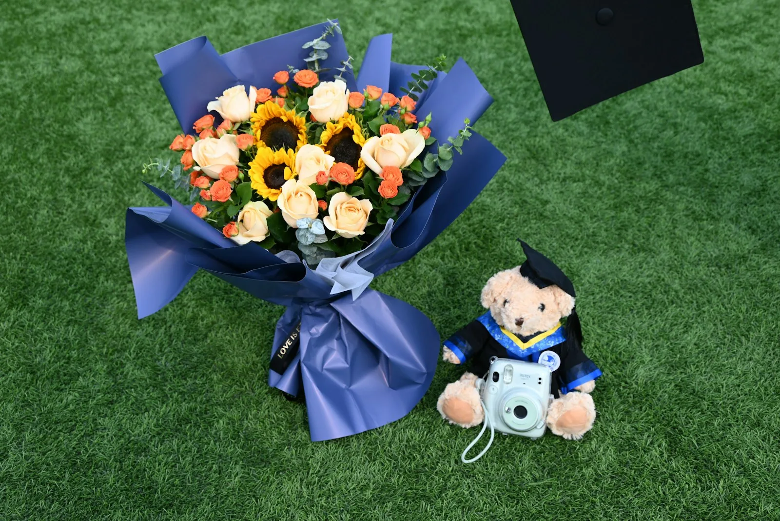 Graduation bouquet, a black cap, and a teddy bear in a cap and gown laid out as keepsakes