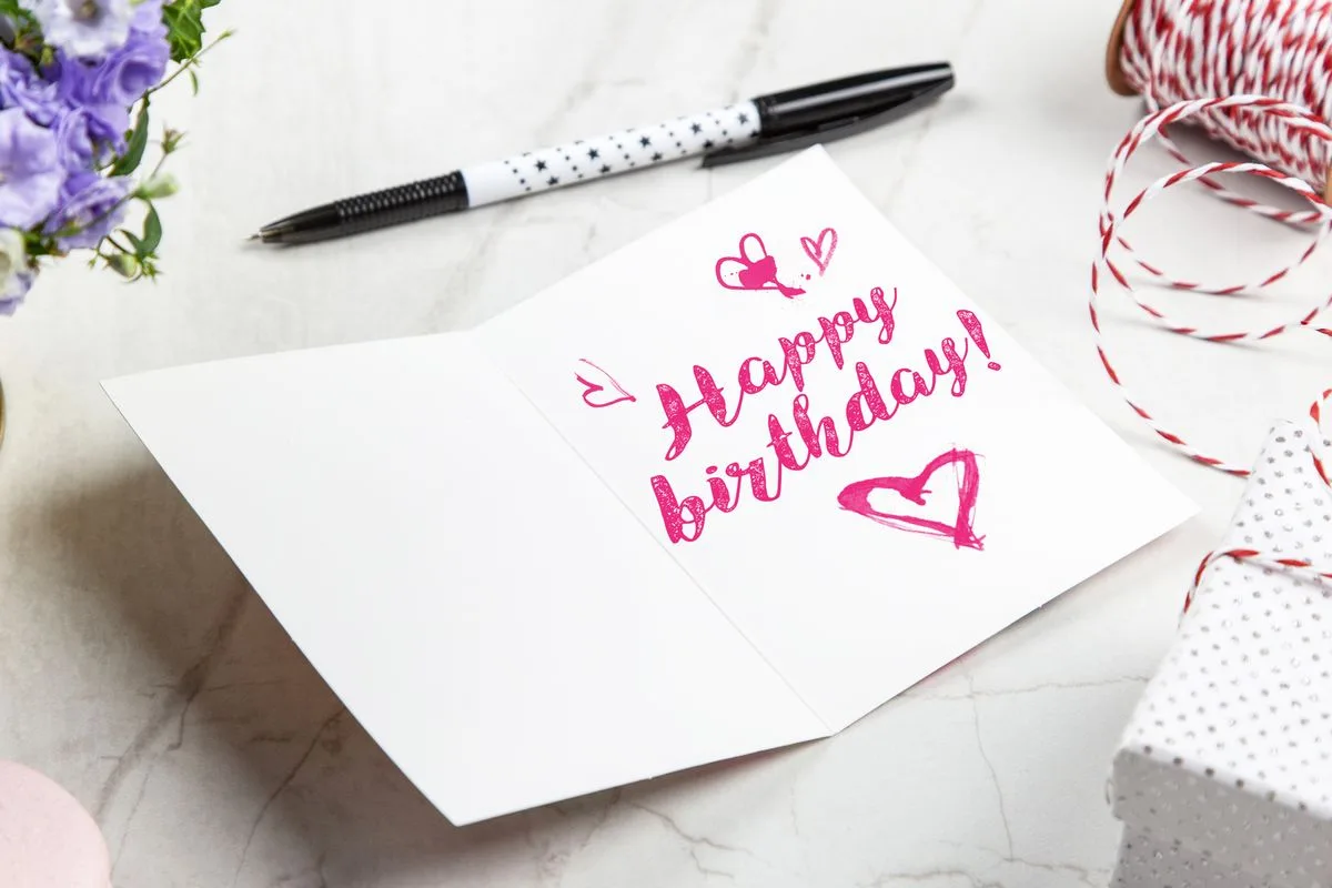 An open birthday card with Happy birthday written by hand in pink, beside a pen and a wrapped gift