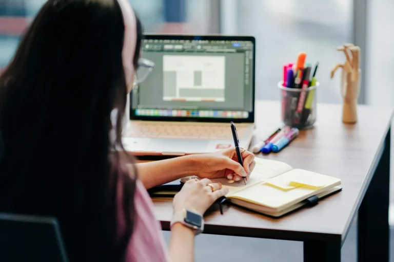 Person designing on a laptop at a bright plant-filled desk
