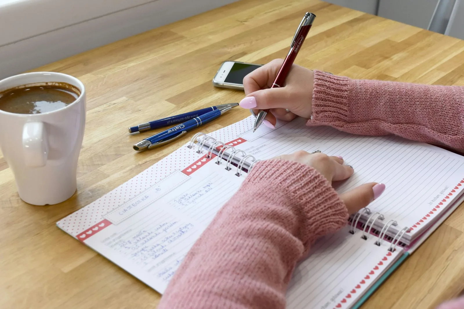 Woman writing money affirmations by hand in a spiral journal with coffee on a warm wood desk