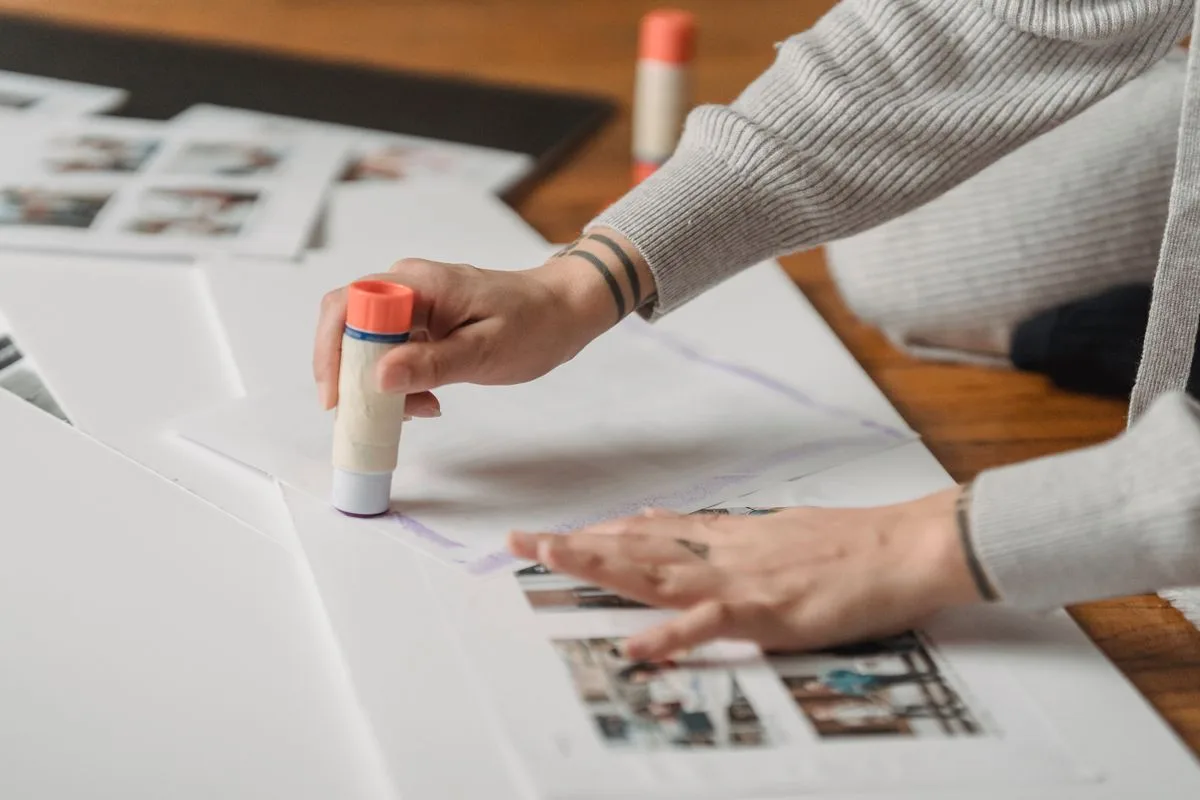 Hands arranging printed photos and keepsakes for a travel scrapbook page