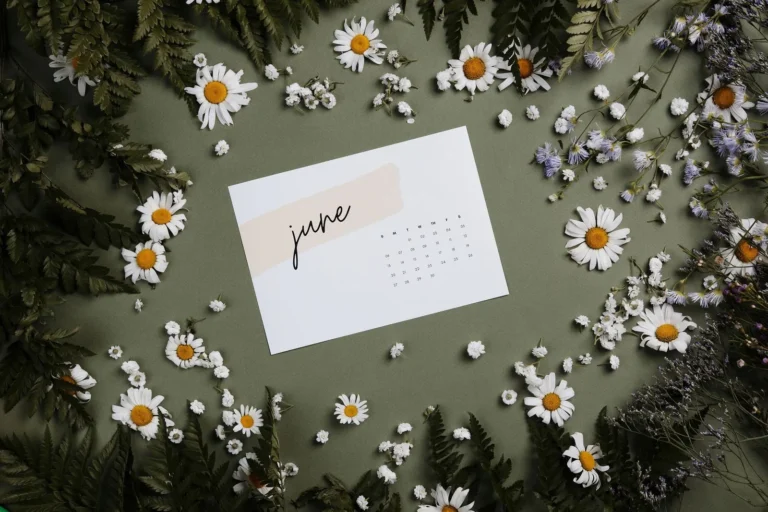 A printed June calendar page on a green table surrounded by daisies