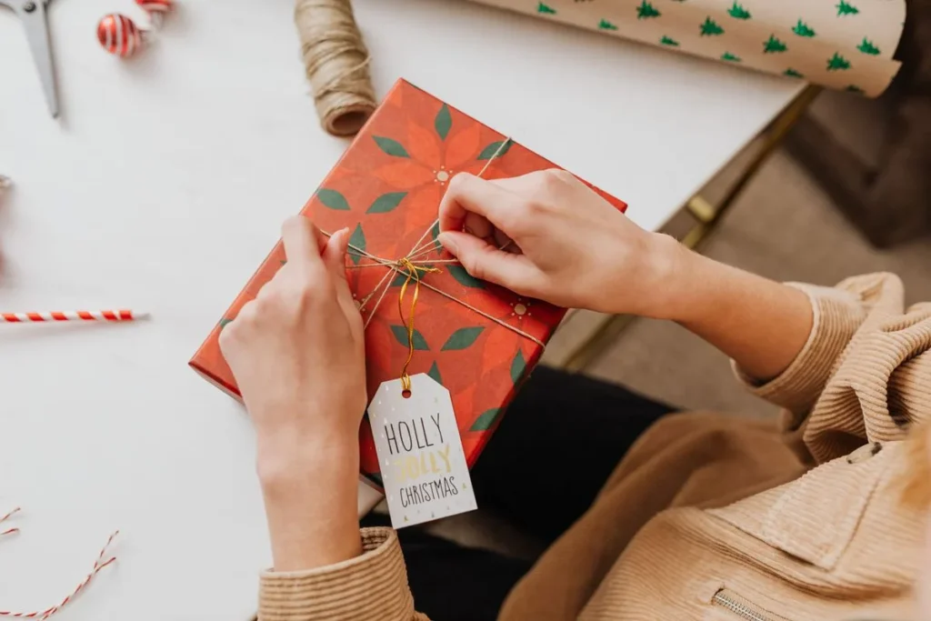Hands wrapping a gift in red patterned paper with a Holly Jolly Christmas tag