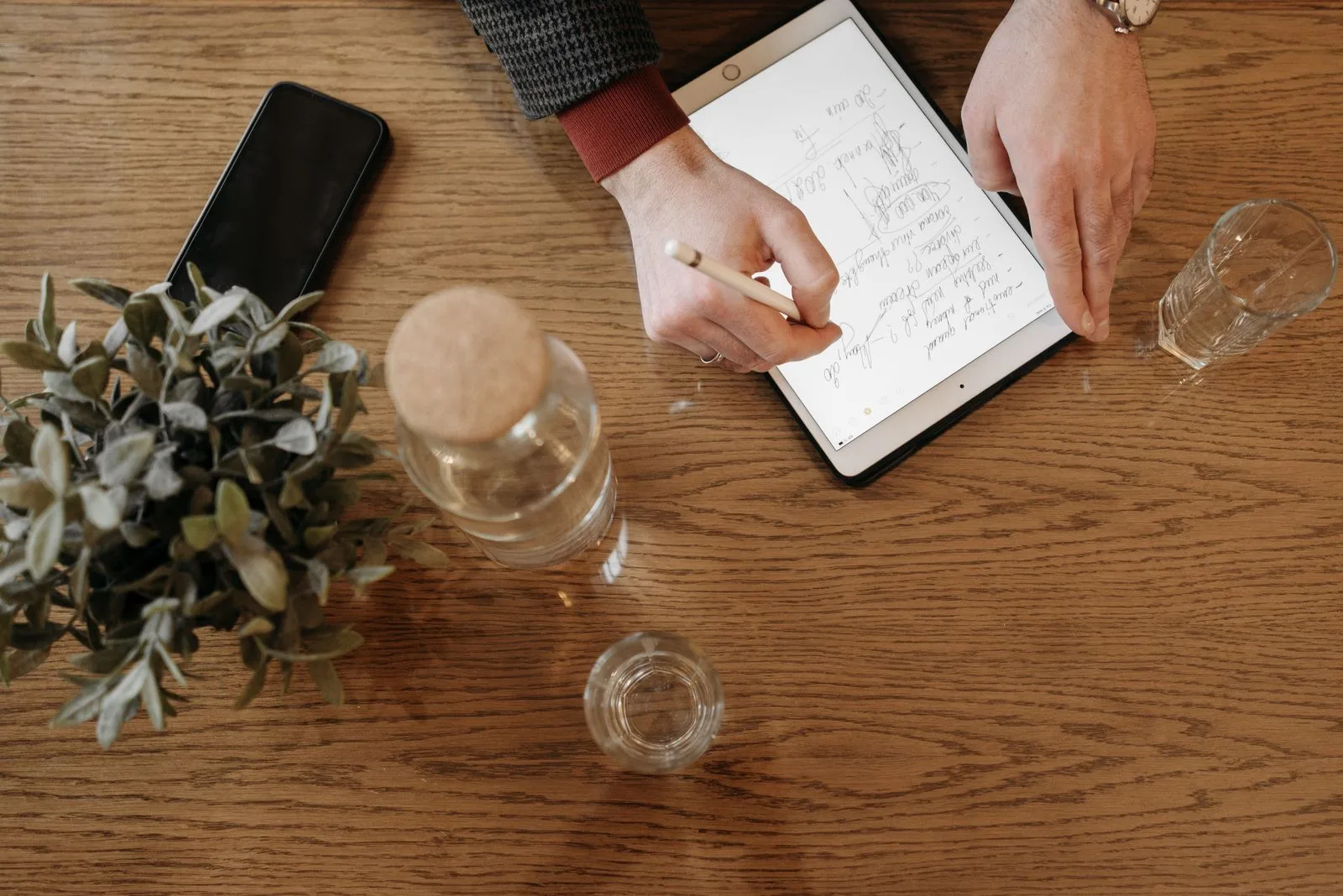 Hands writing notes on a tablet with a stylus at a wooden table