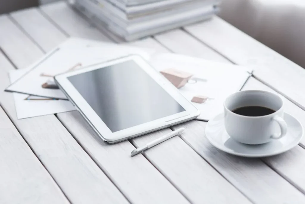 A tablet and stylus on a white table next to a cup of coffee