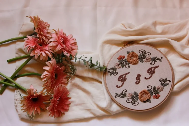 Embroidery hoop with an F and F couple monogram framed by stitched roses, beside pink flowers