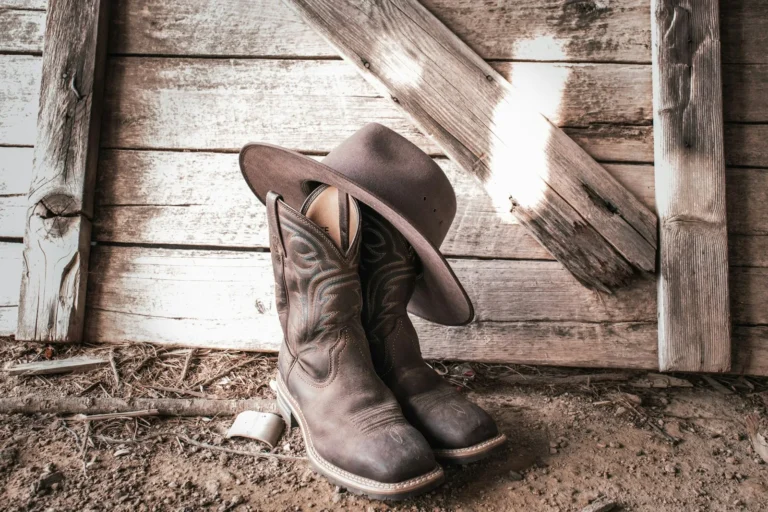 Worn brown cowboy boots and a cowboy hat on the floor of an old wooden barn