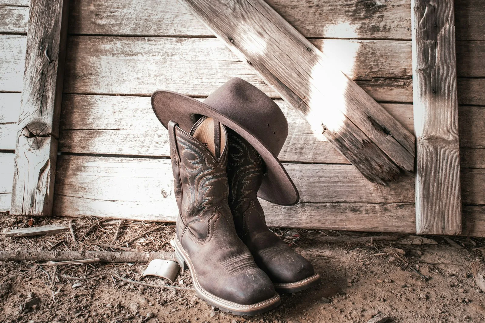 Worn brown cowboy boots and a cowboy hat on the floor of an old wooden barn
